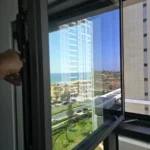 חלון נקי במסגרת כהה עם נוף לים ולעיר